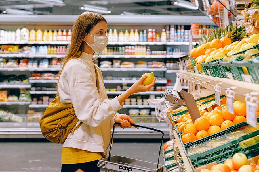 Mulher usando máscara descartável no setor de frutas de um supermercado e segurando um limão Siciliano