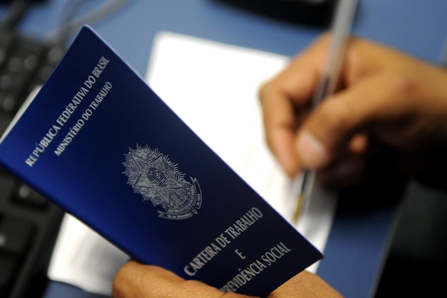 Pessoa segurando a carteira de trabalho Brasileira (CTPS) e fazendo anotações